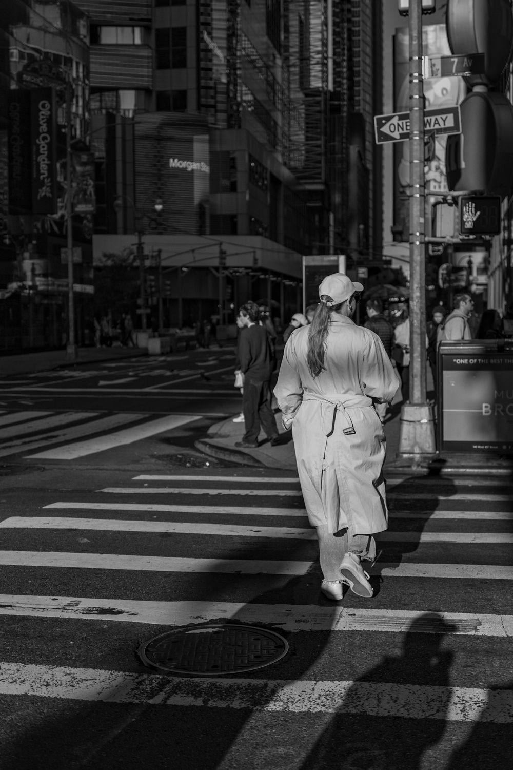 Black and white photo of a pedestrian crossing a city street in casual attire.