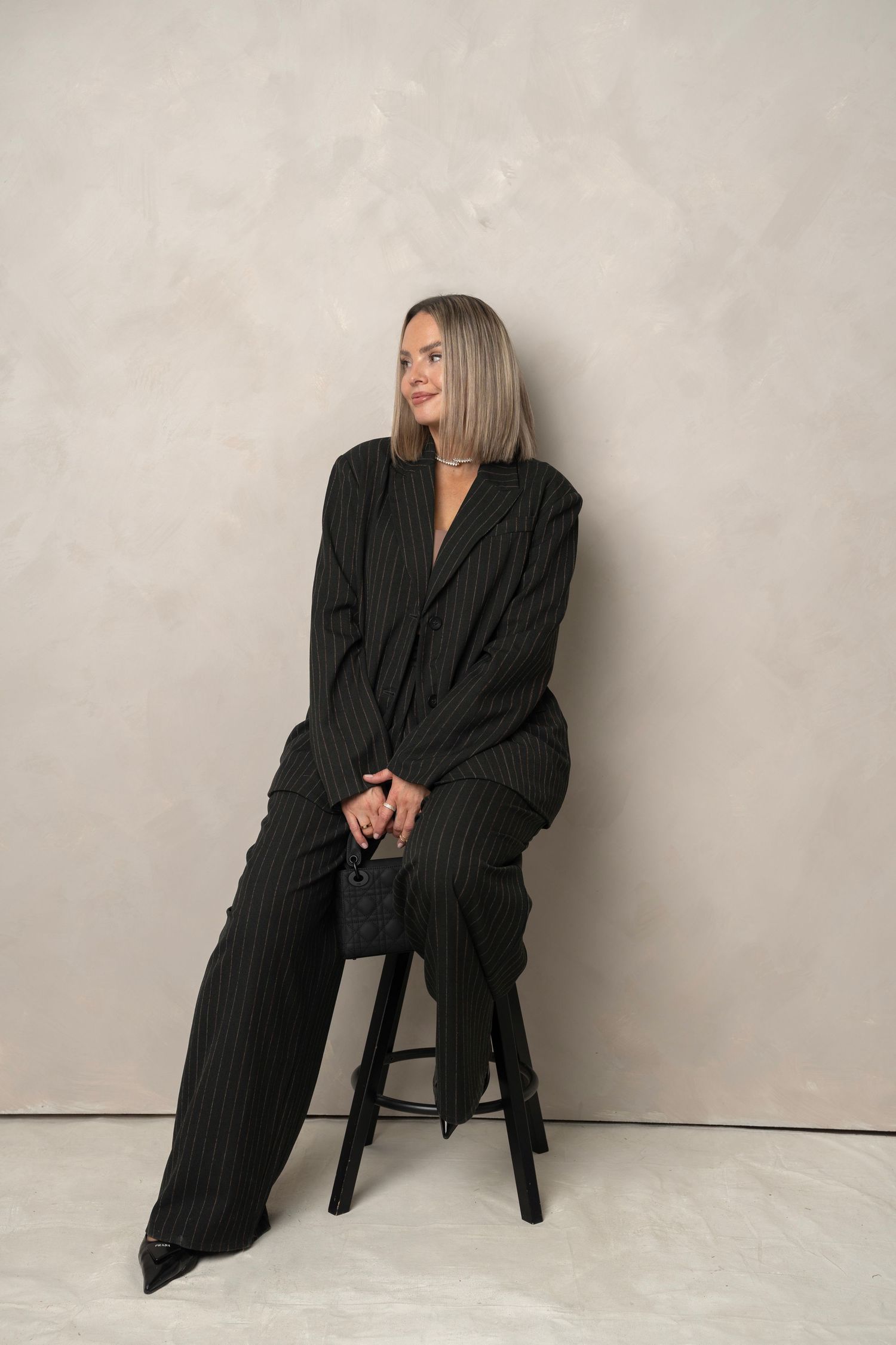Fashionable outfit featuring a black pinstriped pantsuit, pointed heels, and a small handbag against a neutral background.