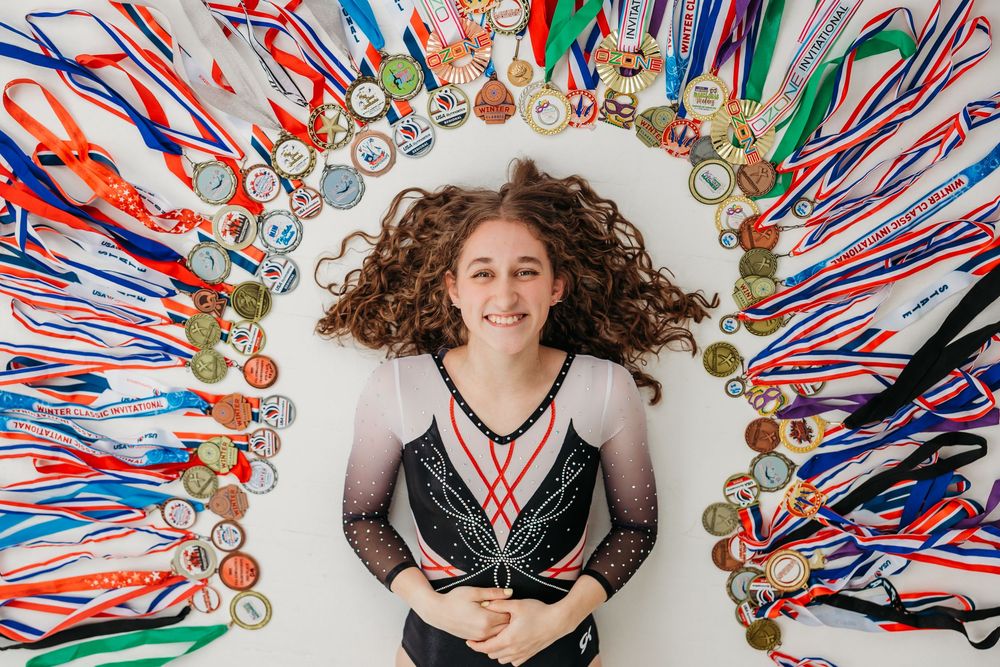Senior gymnast girl posing with all of her gymnastic metals. Cincinnati, Northern Kentucky, and Chicago Portrait Photographer.
