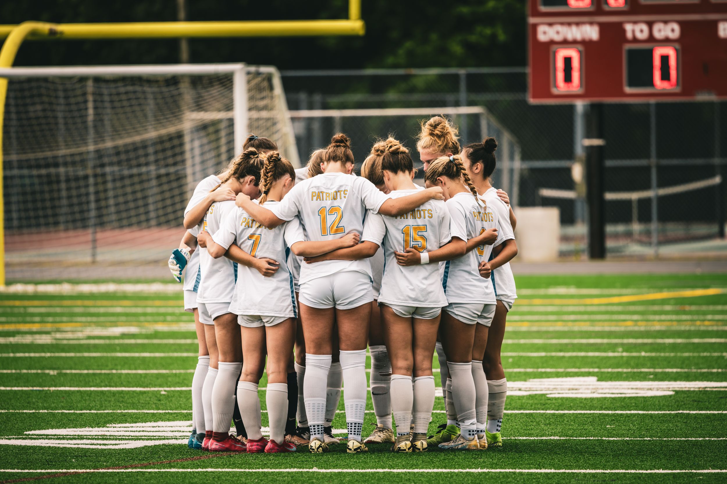 Women's soccer team huddles together on green field before game.
