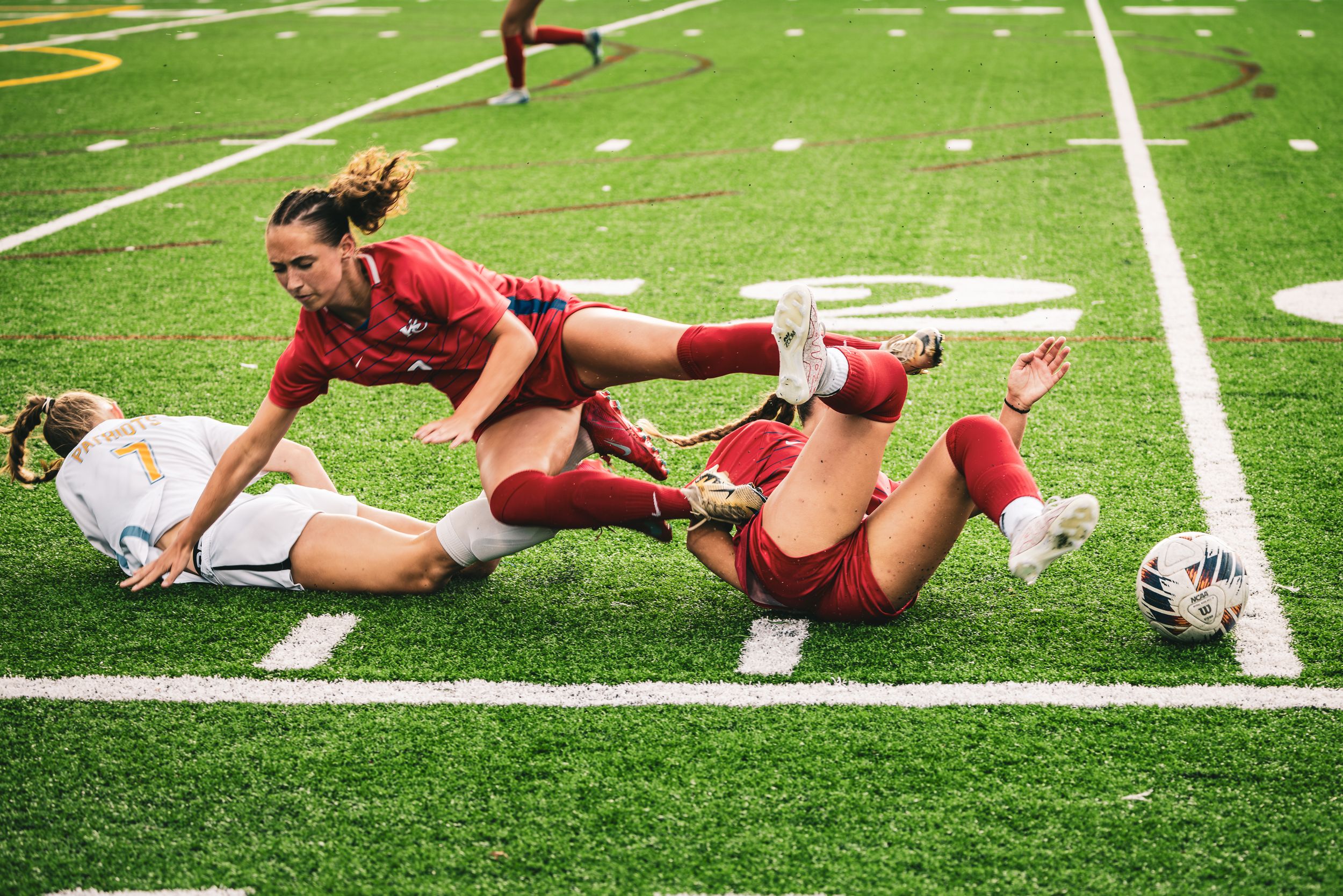 Two female soccer players fall to turf during intense match competition.