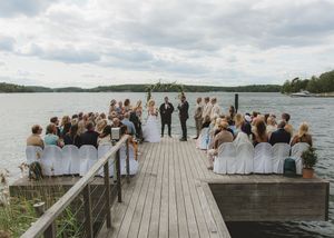 Outdoor lakeside wedding ceremony on wooden dock with seated guests and scenic water backdrop.
