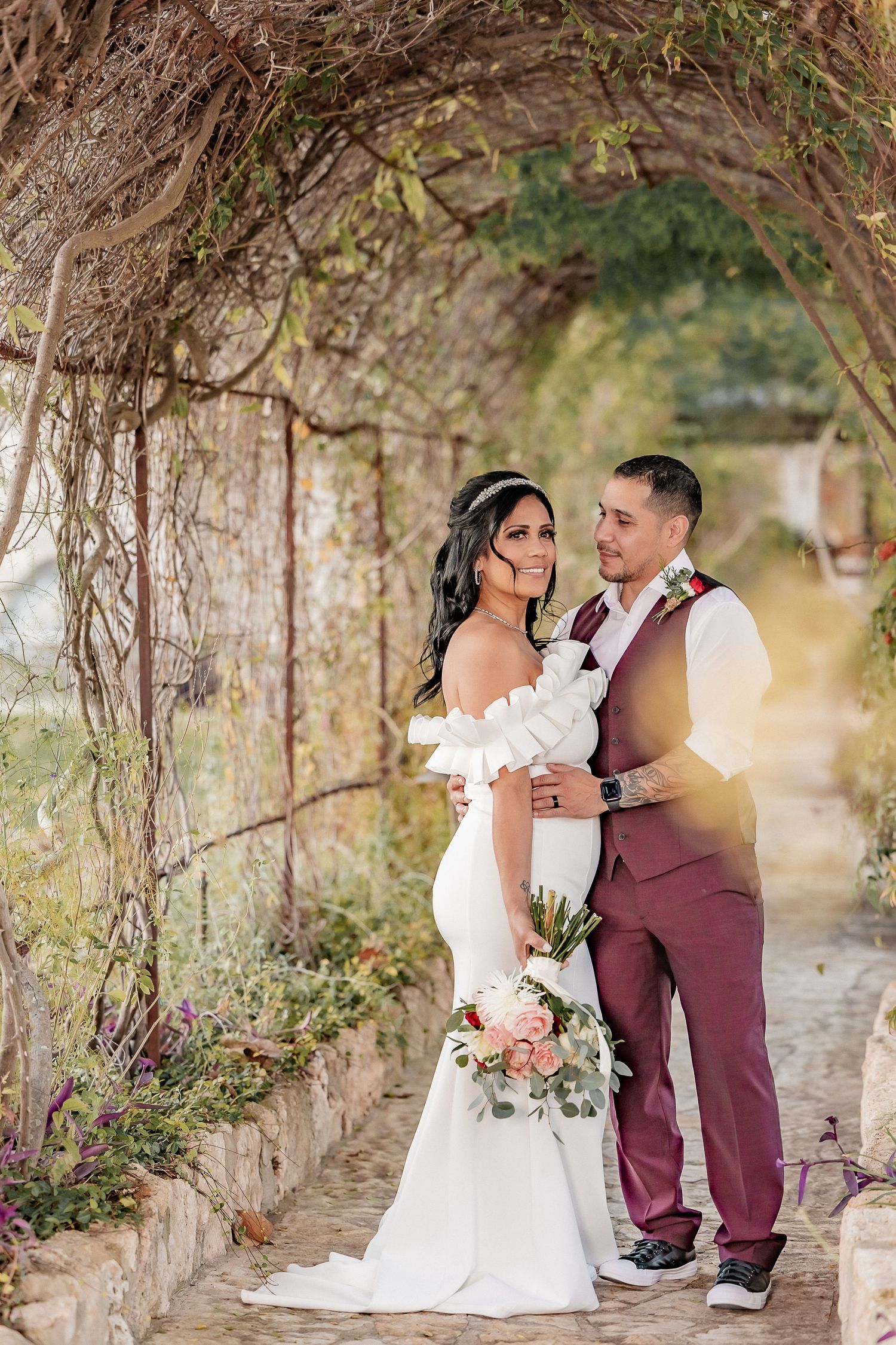 A wedding couple poses together under an elegant ivy-covered garden arbor in soft natural light.