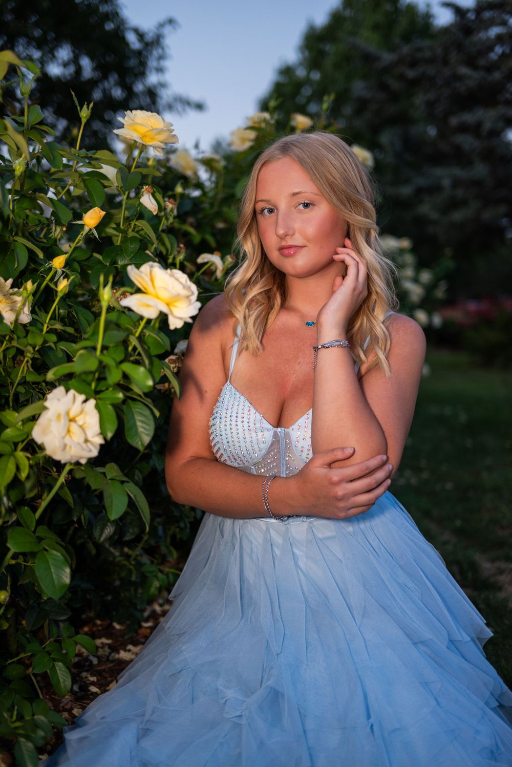Elegant light blue tulle gown and white top photographed in garden setting with blooming yellow roses.