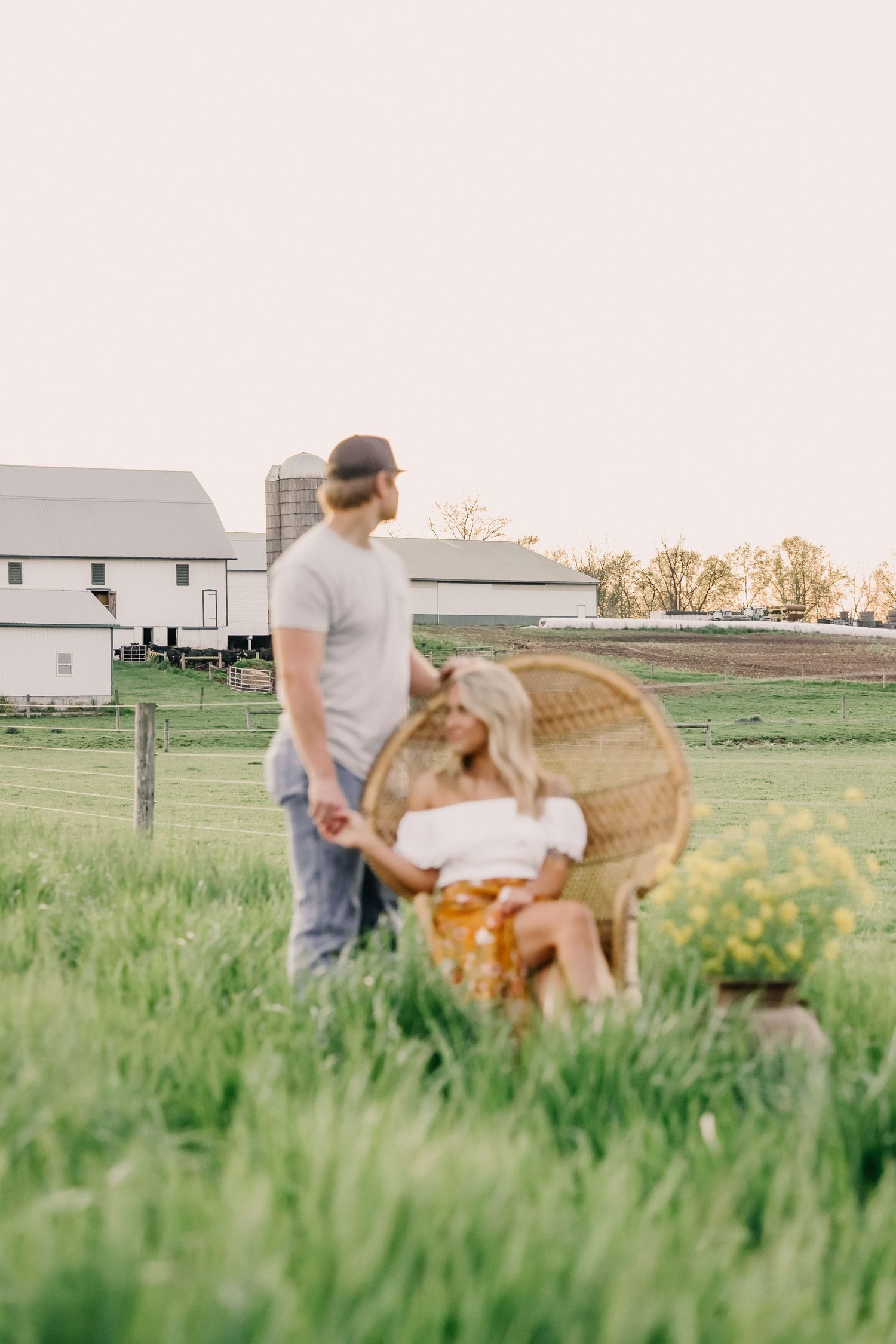 Couple sharing intimate moment on farm with barn and dog in golden evening light.