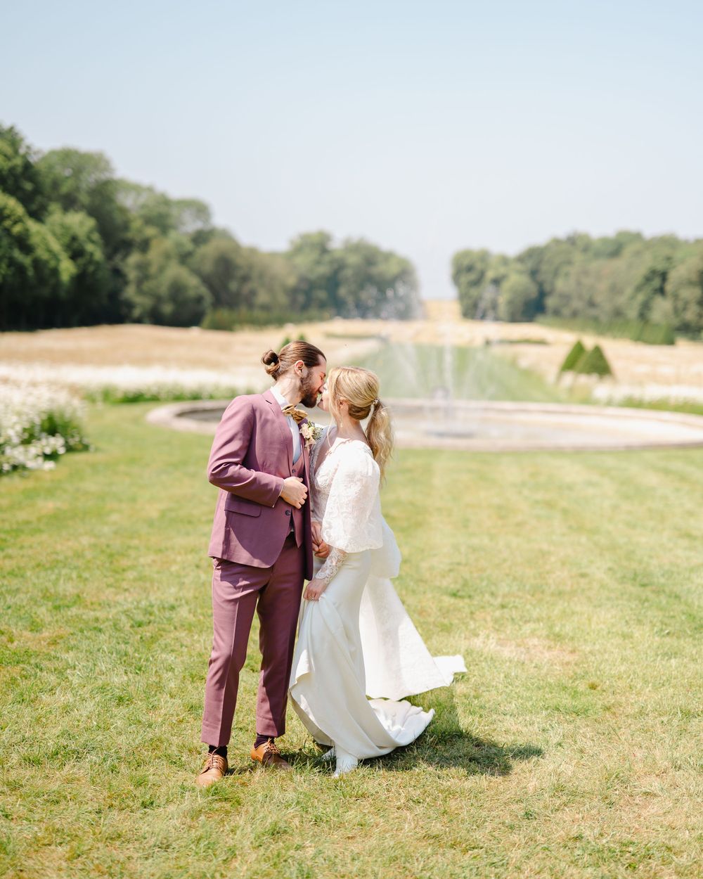 Wedding couple standing in a picturesque garden with a fountain in the background.