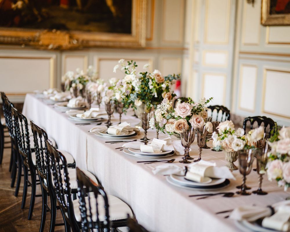Long wedding reception table with white linens, black chairs, and delicate floral centerpieces.