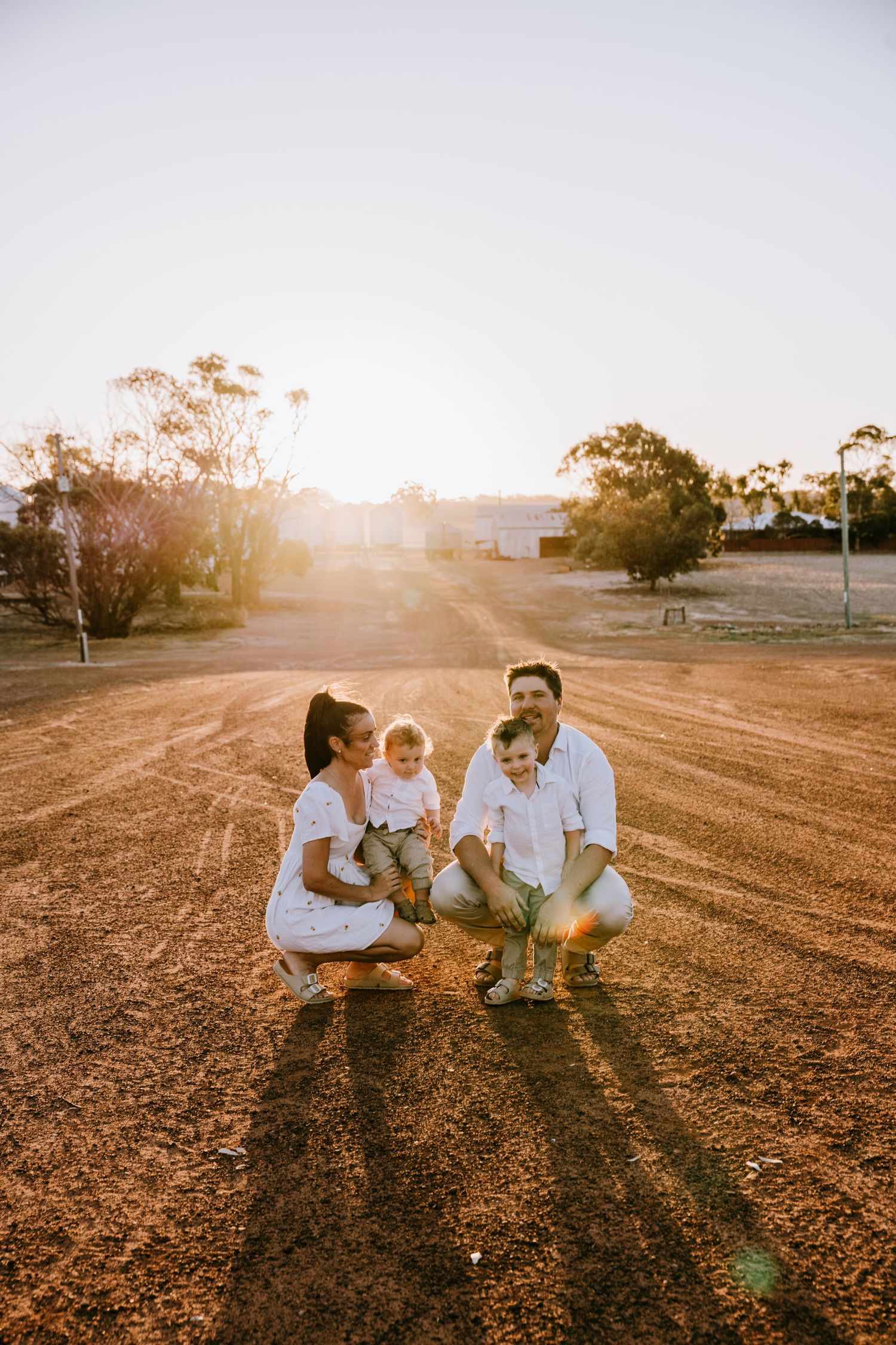 Family sitting together on desert terrain during sunset photoshoot wearing coordinated white outfits.