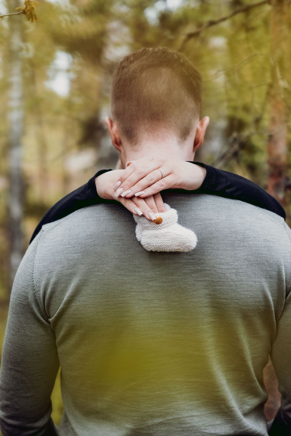Back view of person in grey sweater wiping tears with tissue outdoors.