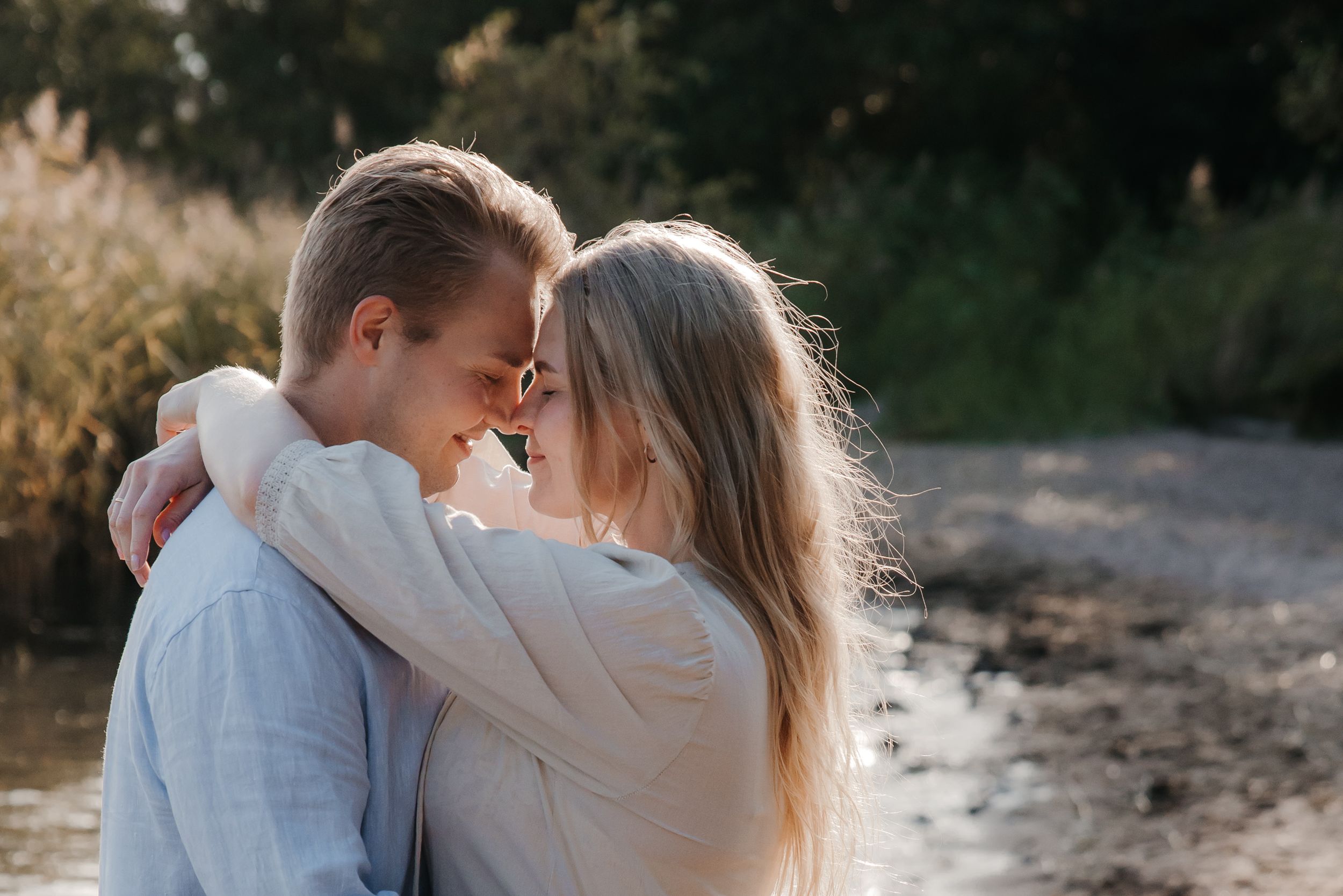 A romantic couple shares intimate moments by the water during a sunset photo session.