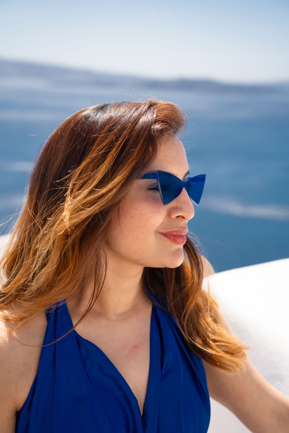 Stylish figure in blue dress and cat-eye sunglasses enjoying Mediterranean coastal views.