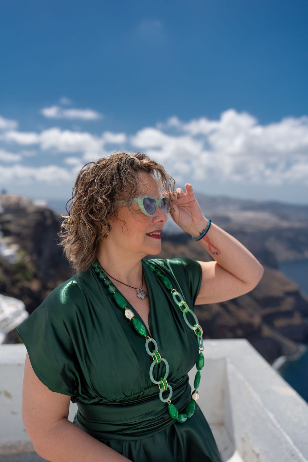 Green-dressed figure enjoying scenic Santorini views from whitewashed terrace overlook.