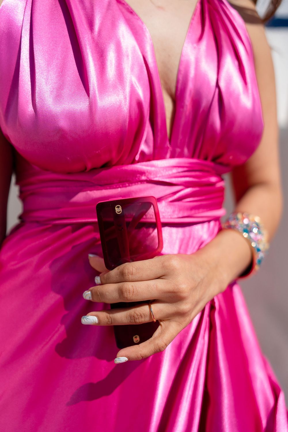 Close-up of hands holding phone wearing pink satin dress with pleated bodice.