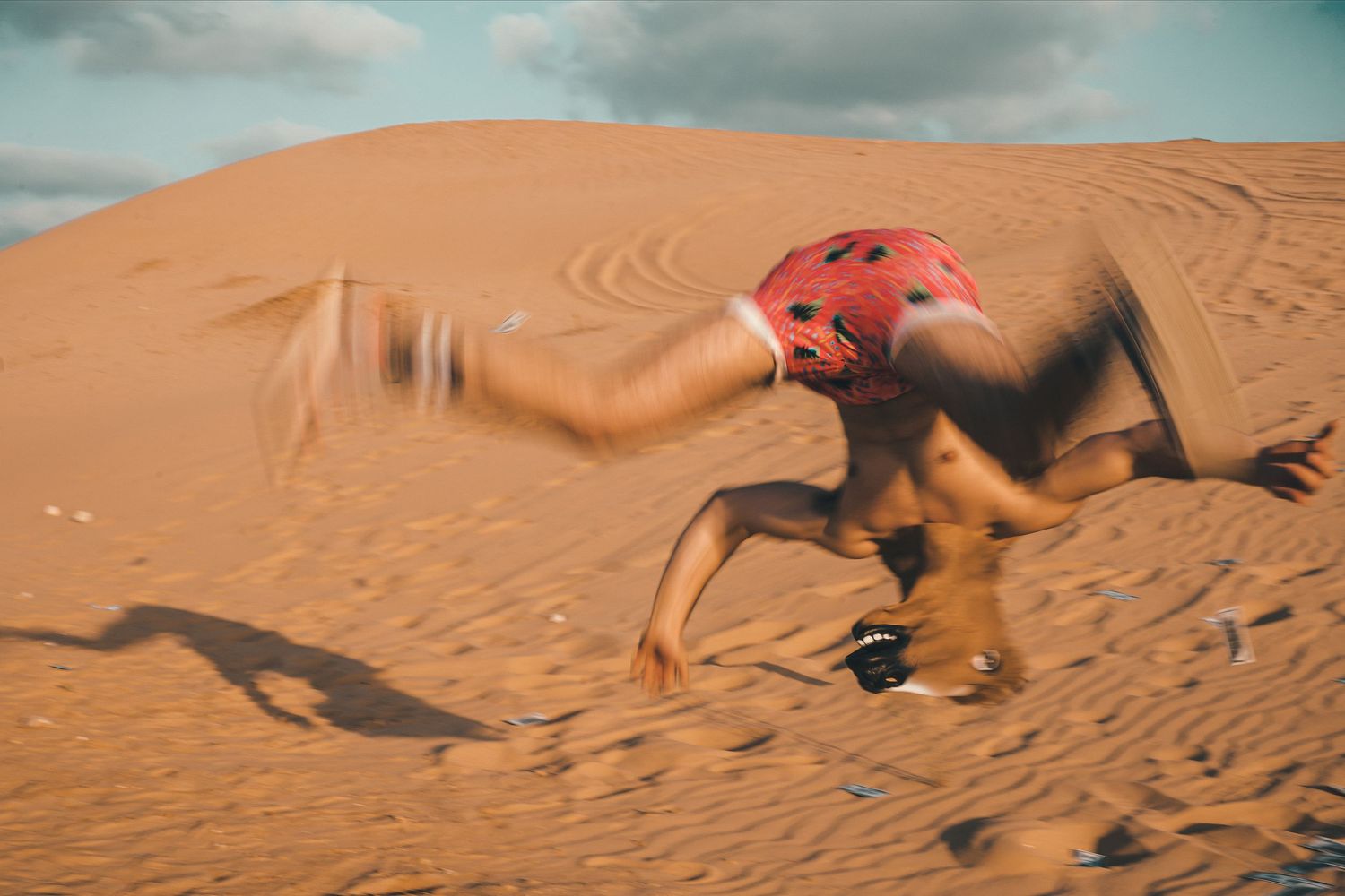 A motion-blurred figure in red runs across desert sand dunes.