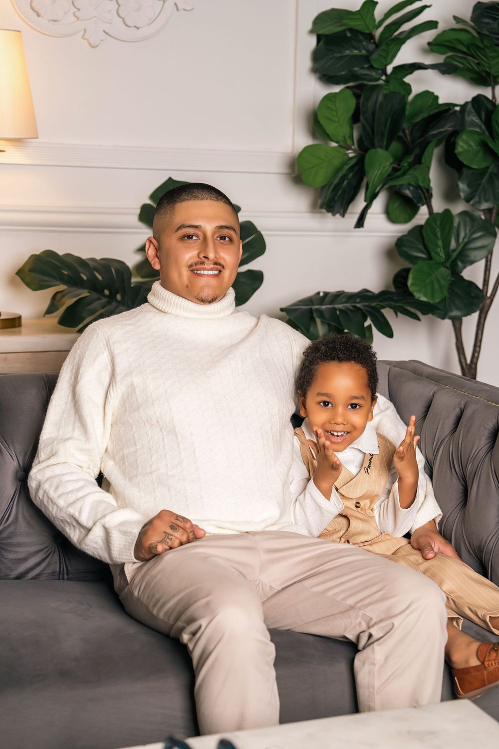 Portrait of two people sitting on grey couch in white room with tropical plants.