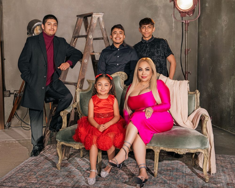 A family in formal attire poses together on a gray sofa in a studio setting with industrial decor and lighting equipment.