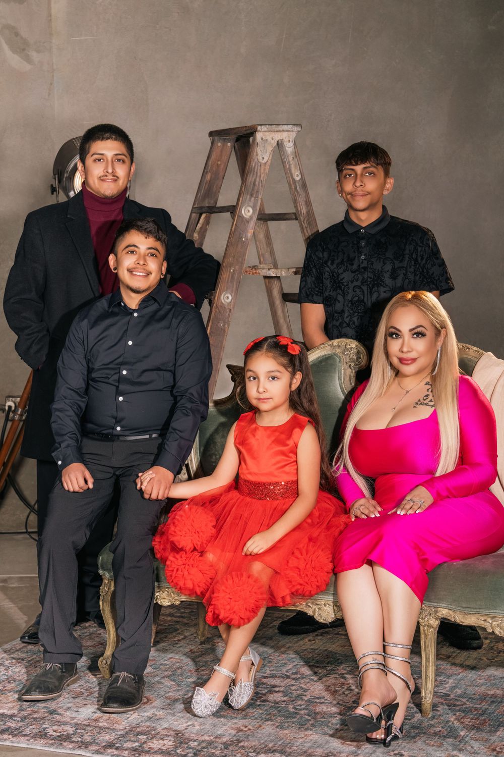 Family portrait with ladder backdrop showing group in formal attire including bright red dress and hot pink gown.