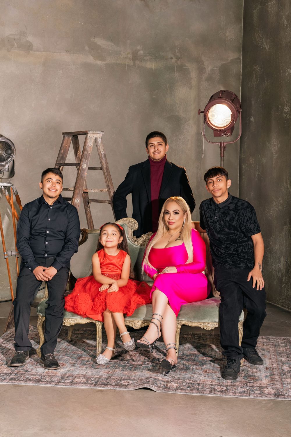 A family poses together in a studio setting with an industrial backdrop, wooden ladder, and vintage light fixture.
