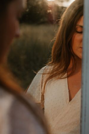 Woman in white textured dress poses in soft evening light outdoors.