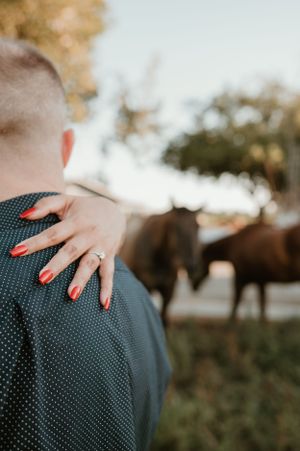 Close-up of hand with red nails resting on shoulder during outdoor photoshoot.