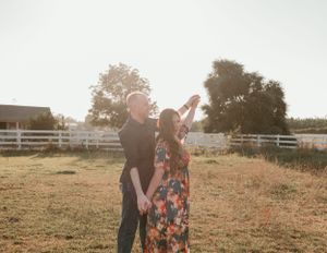 Couple sharing romantic moment in field with white fence during sunset.