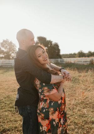 A couple embraces in a sunlit field wearing casual and floral attire.