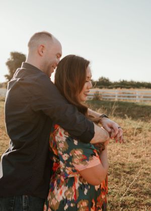 Romantic couple embracing in floral dress and dark jacket during golden hour photoshoot.