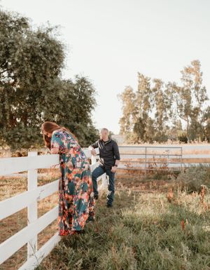 Couple walking along white fence during sunset photoshoot in rural setting.