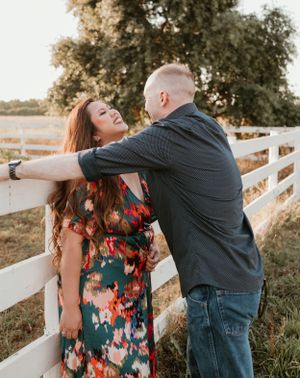 Romantic couple sharing an intimate moment against a white fence during golden hour sunset.