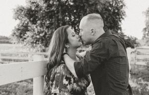 A romantic couple shares intimate moments by a white fence during sunset.