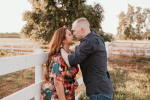 Romantic couple embraces in warm sunset light by white fence during outdoor photo session.