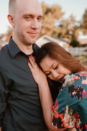 Couple embracing in tender moment by rustic fence during sunset photoshoot.