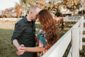 Couple poses lovingly against white fence during countryside photoshoot at sunset.