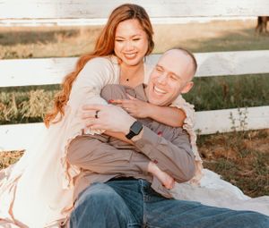 A couple laughs together while relaxing outdoors in golden hour light.