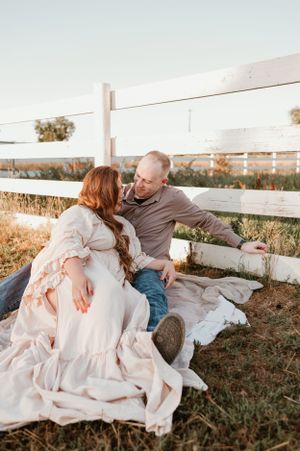 Couple sitting together on blanket by white fence in rustic setting.