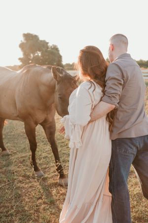 Couple and horse share intimate moment in sunlit farm field.