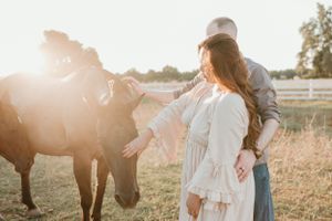 Couple pets brown horse during sunset engagement photo session.