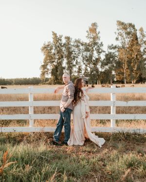 Couple walking along white fence in golden afternoon light.