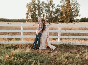 A couple enjoys a romantic moment by a white fence at sunset.