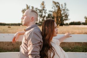 A couple shares tender moments while sitting by a white fence at sunset.