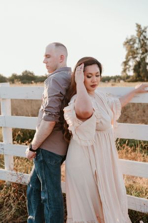 A couple dances together by a white fence at sunset in a romantic countryside setting.