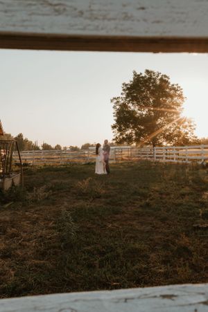 A rustic farm scene at sunset with white fencing and trees silhouetted against the sky.
