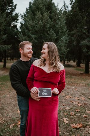 Couple in autumn setting sharing a tender moment while holding ultrasound photos.