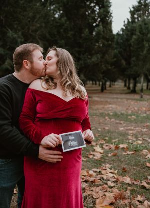 Intimate moment between couple in red dress and black shirt holding sonogram photos.