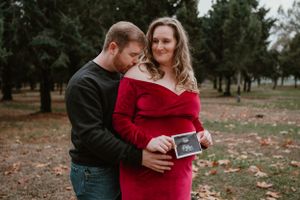Couple embracing in wooded area while displaying ultrasound photos.