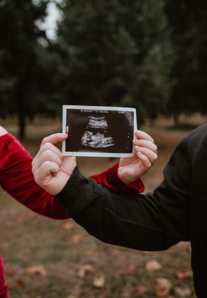 Close-up of hands holding ultrasound photos against fall foliage background.