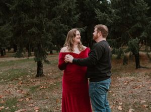 A couple embraces in an autumn forest setting with fallen leaves and evergreen trees.