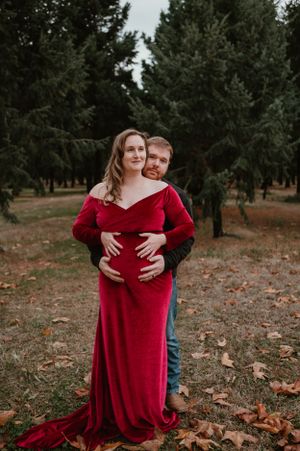 Two people share an intimate embrace while standing among pine trees and fallen leaves.