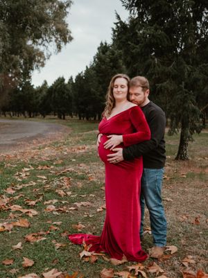 A tender outdoor photoshoot in a forest with autumn leaves scattered on the ground.