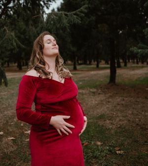 Person in a vibrant red velvet dress poses elegantly in a forest setting.